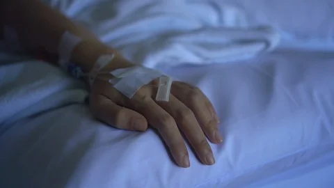 Close up IV drip solution in a patient's hand while lying on bed in hospital. Stock Footage