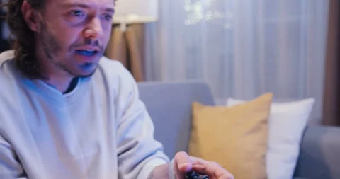 Close up of joyful young man sitting on comfortable couch and using joystick for Stock Footage 244144314