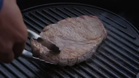 Close up of juicy beef steak flipped around with tongs on hot grill Stock Footage 276742904