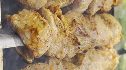 A close-up of juicy pork kebabs being grilled over a fire outdoors. Vertical Stock Footage 250352342