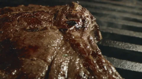 Close up of a juicy t-bone steak sizzling on a hot grill with charred sear marks Stock Footage 341762694