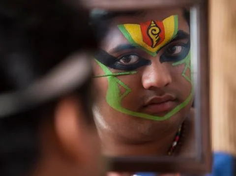 Close up of a Kathakali dancer looking in the mirror and applying green colour o Stock Photos