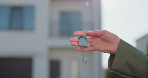 Close-up of a key with a house-shaped keychain in hand. In the background is a Stock Footage 309090817