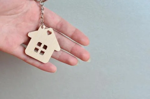 Close-up of a keychain in the shape of a house in hands. Gray background. Stock Photos