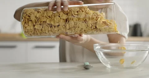 Close-up kid girl prepares corn flakes for breakfast, pours into a bowl. Cereal Stock Footage 267024708