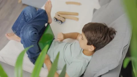 Close up kid lying on sofa, holding and tapping on a tablet with green screen. Stock Footage 255510974