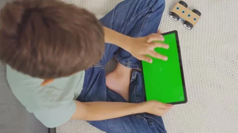 Close up kid sitting on sofa, tapping on a tablet with green screen. Chroma key Stock Footage 255510728