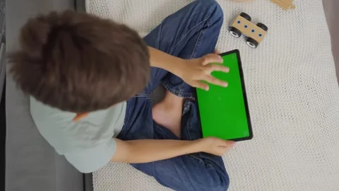 Close up kid sitting on sofa, tapping on a tablet with green screen. Chroma key Stock-Footage 275555900