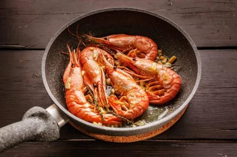 Close-up King prawns fried in a ceramic pan on a dark wooden table Foto stock