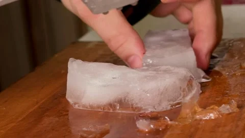 Close up of a kitchen knife cutting a melting ice block on a wooden surface Stock Footage 339848173