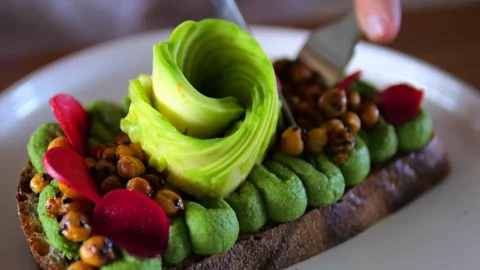 Close-up knife and fork cutting toast with avocado, vegetables and legumes Stock Footage 276362338