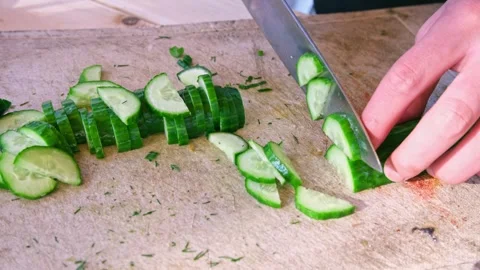 Close-up of a knife cutting a long cucumber on a wooden cutting board. Picnic Stock Footage 240750630