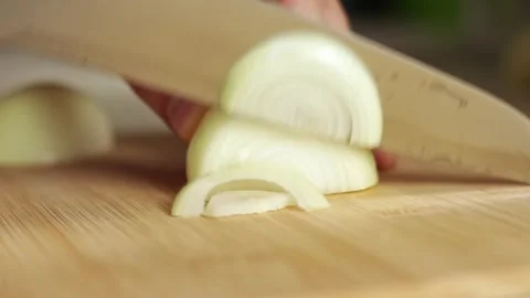 Close-Up of Knife Cutting Onions into Half Rings on Wooden Board Stock Footage 256602848