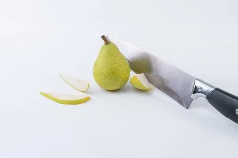 Close-up of a knife cutting a slice of pear accompanied by a whole green pear Stock Photos