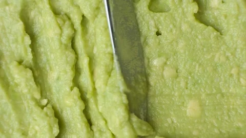 Close-up of a knife scraping fresh green guacamole texture to create copy space. Stock Footage 340549715