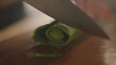 Close-Up of Knife Slicing Fresh Leek on Wooden Cutting Board Stock Footage 292575379