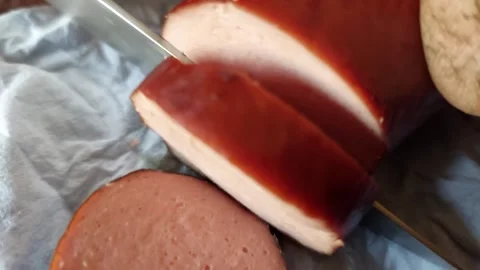 Close-up of a knife slicing a fresh smoked homemade sausage on a paper Vídeos de archivo 333642953