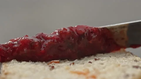 Close-up of a knife spreading red jam on bread. with a picnic in nature Stock Footage 165974945