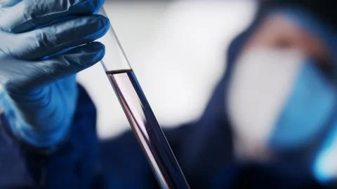 Close up . Lab assistant in protective suit studying sample in laboratory glass Stock Photos