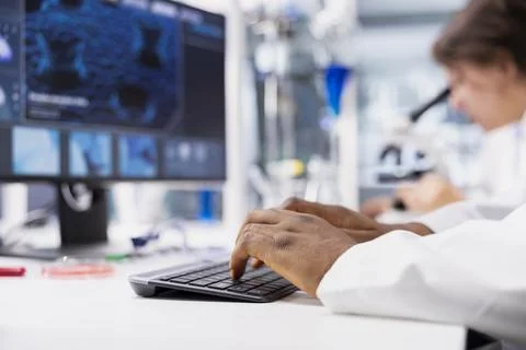 Close up of lab technician typing on PC keyboard, looking at 3D molecular model Stock Photos