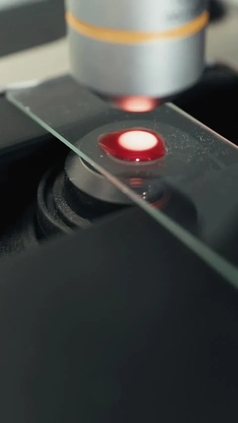 Close-up of laboratory microscope focusing on a glass slide with a red liquid Stock Footage 340340901