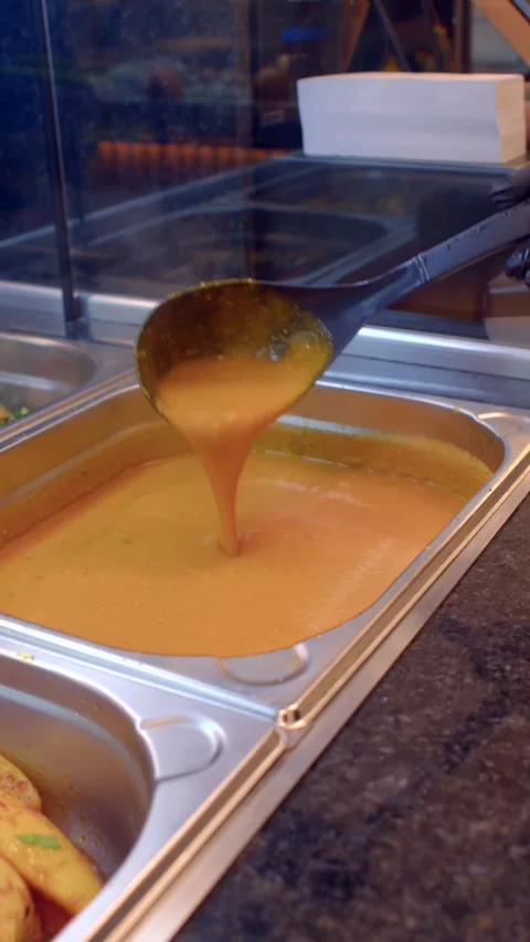 Close-up of ladle dipping orange soup in stainless steel steam table pan at Vidéo 336534185