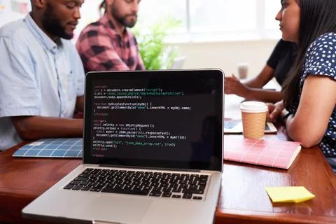 Close up of laptop screen with code, developers meeting boardroom table talking Stock Photos