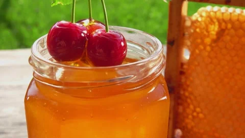 Close-up of large cherries on the twig dipped into fresh honey in a glass jar Stock Footage 160961785