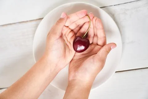 Close-up of a large cherry in the shape of a heart in the hands of a girl Stock Photos