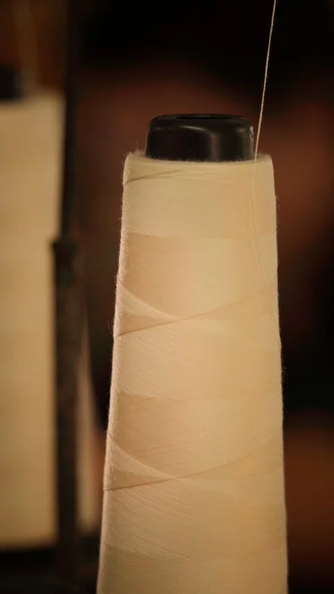 Close-up of a large cone spool of light beige spun polyester thread being u.. Stock Footage 342492135