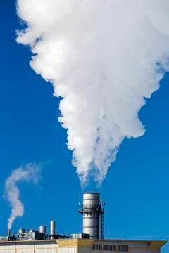 Close-up of large metal factory stack with large steam exhaust against a blue sk Stock Photos