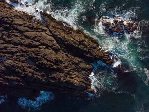 Close-up. Large rough boulder in the ocean. White foamy waves crash against t Stock Photos