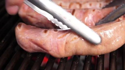 Close-up of a large sausage grilling on a BBQ with tongs Stockbeeldmateriaal 331955123