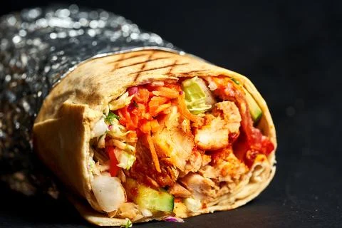 Close-up on a large shawarma with meat, vegetables and sauce on a dark backgr Stock Photos