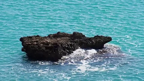 Close-up of a large stone on the sea. Waves crash against the stone. Turquoise Stock Footage 247501418