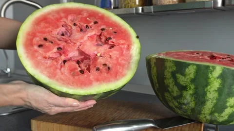 A close-up of a large watermelon, cut in half, being held by a woman. Stock Footage 337702863