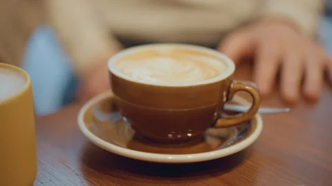 Close up of latte in brown ceramic cup on wooden table with yellow mug beside Vidéo 346734112
