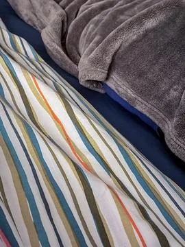 Close-up of layered bedding — a striped multicolor duvet beneath plush blanket Stock Photos