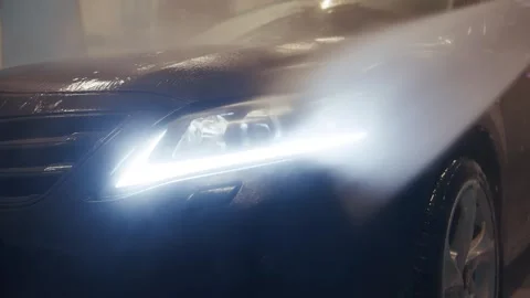 A close-up of a led headlight on a black car by a jet of pressurized water Stock Footage 316415678