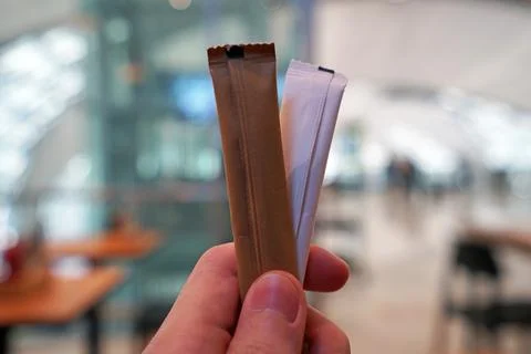 Close up left hand holding stick packets of brown and white sugar  Stock Photos