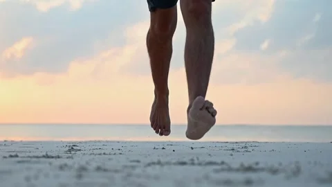 Close-up of the leg of an athletic young man running barefoot on the sandy shore Stock Footage 243857016