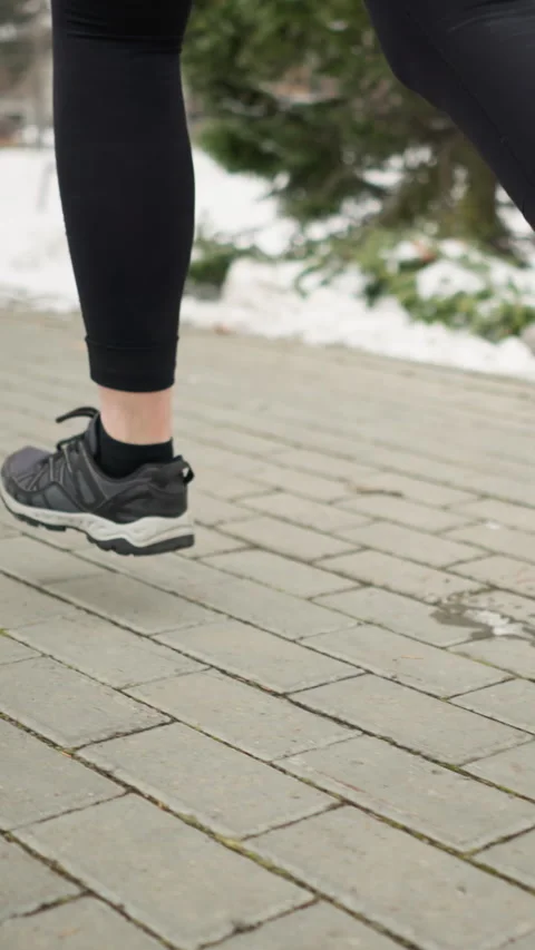 Close-up leg view of lady jogging on paved winter pathway with blurred trees Видео 316594427