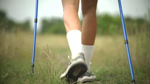 Close-up of legs stepping forward with trekking poles along grassy meadow trail Stock Footage 313951295
