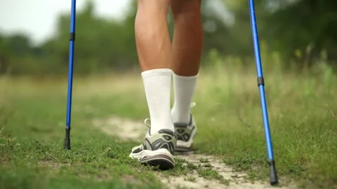 Close-up of legs using trekking poles on grassy trail through meadow Stock Footage 313951296
