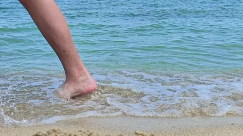 Close-up of legs walking through ocean waves on sand Stock Footage 341750669
