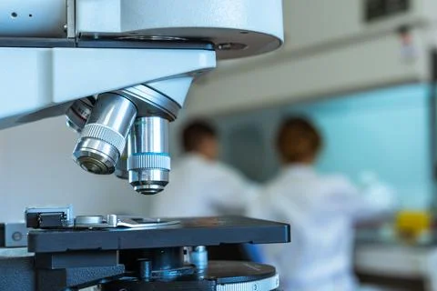 Close up of the lenses of a microscope with two scientists working on the bac Stock Photos