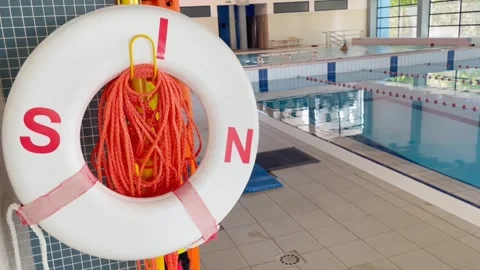 Close-up of life preserver on swimming pool wall and relaxing visitors in the ba Stock Footage 282726574