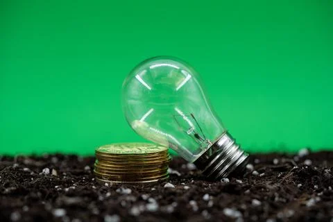 Close up of light bulb and stacked Bitcoin coins on soil with green background Stock Photos