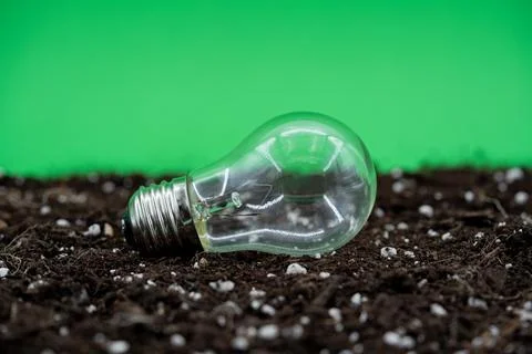Close up of light bulb lying on soil with green background Stock Photos