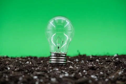 Close up of light bulb standing on soil with green background Stock Photos
